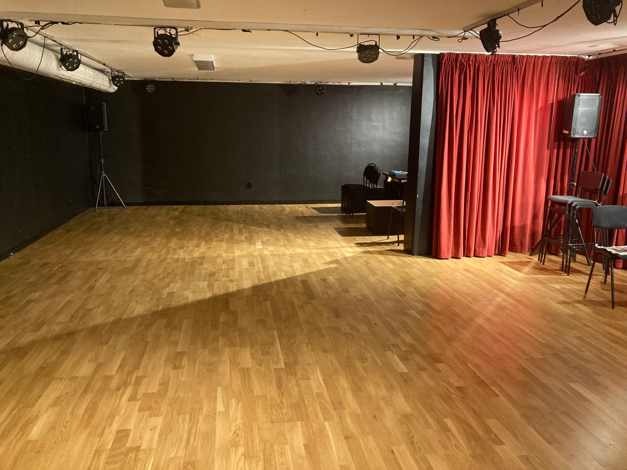 Dramasal med ridå, mörka väggar, parkettgolv och spotlights