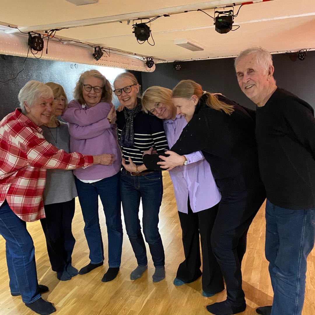 Ett gäng glada seniorer som håller om varandra i teatersalen.